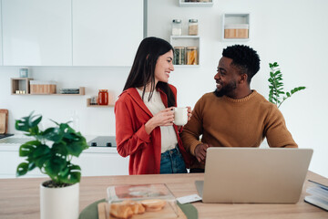 Diverse couple smiling, drinking coffee in kitchen
