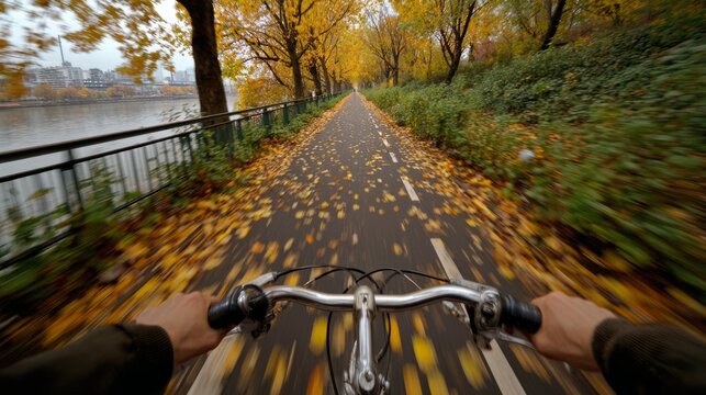 A cyclist rides through a tree-lined path covered in autumn leaves. The scene captures the vibrant colors of fall foliage along the water's edge.