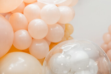 Soft pastel balloon decor in peach and white tones. Close-up shot with glossy transparent balloon in foreground. Gentle light and airy festive atmosphere.