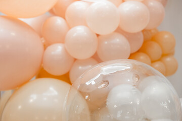 Pastel balloon decoration with blush, peach and white balloons. Close-up festive backdrop with a transparent balloon in the foreground. Soft light, elegant celebration decor.