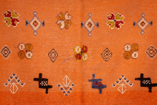 Detailed texture of an orange Moroccan Berber carpet featuring tribal symbols. Close-up of a traditional Berber rug with colorful handwoven geometric motifs. - Powered by Adobe