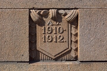 Stone carving is a detail from Pitkäsilta (Long Bridge) granite bridge, the dates A.D. 1910-1912 on the shield mark the years of its construction, Helsinki, Finland.