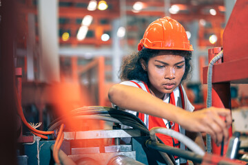 Professional Black African female factory engineer/worker/technician operate machinery in modern industrial plant. She wear safety helmet,vest show focus,skill in repair maintenance production process