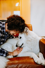 A tender moment as a man rests her head against her white dog while relaxing on the couch. Love and trust between human and pet.