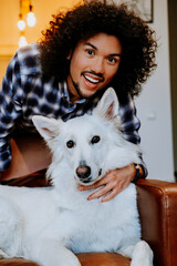 A joyful young man snuggling her white dog indoors on a cozy couch. A warm moment of love and companionship.