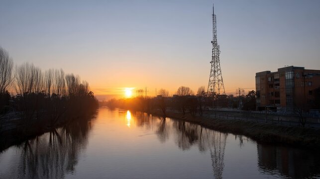 Serene city skyline at sunset with fiery sky reflection on tranquil river and silhouette of radio tower, urban environment with modern buildings and peaceful ambiance - Powered by Adobe