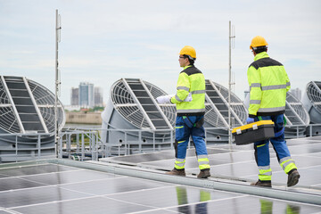 Back view construction workers walking on a rooftop solar panel array, one carrying a blueprint, another with a toolbox. They wear safety gear, indicating a professional environment