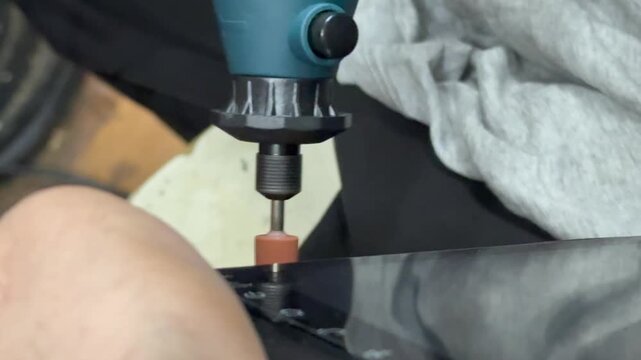 Craftsman hands processing material edge with a high speed rotary dremel tool in a workshop. Electric rotary tool grinding a smooth surface edge close up. 