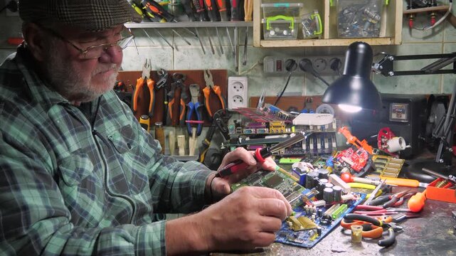 An elderly technician repairs computer equipment in a workshop using measuring instruments and technical tools. Slow motion.