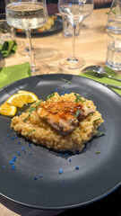 Delicious chicken fillet with rice risotto and sauce served on a black plate in a small home restaurant with glasses in the background