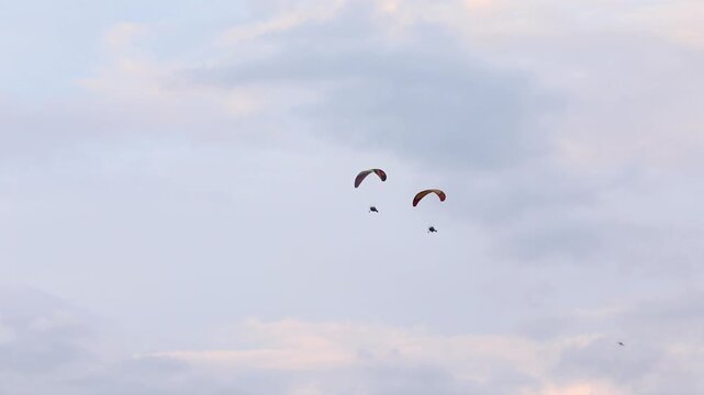 A motorized paraglider (paramotor/powered parachute) flies across a cloudy sky, towing a white advertising banner. Recreation, extreme sport, and aerial advertising activity.