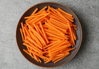Freshly cut carrot sticks in a dark bowl, healthy eating ingredients, raw food preparation
