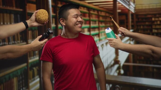 Man smiling with eyes closed while hands hold sponge razor and shampoo bottle in library building; playfulness curiosity.