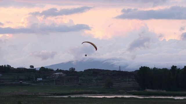 A motorized paraglider (paramotor/powered parachute) flies across a cloudy sky, towing a white advertising banner. Recreation, extreme sport, and aerial advertising activity.
