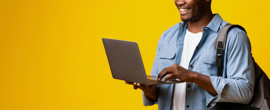A young man stands confidently with a laptop, smiling as he interacts with the device. The bright yellow background adds a cheerful tone to his focused expression. - Powered by Adobe