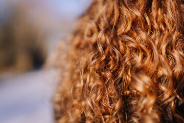 Close-up view of vibrant curly red hair, showcasing the texture and shine, with a blurred natural background, emphasizing the beauty of natural hairstyles and individuality