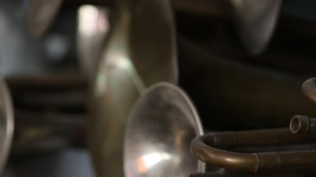 A close-up view of numerous brass instrument bells, possibly trumpets or cornets, stacked together. The aged metal reflects light, showcasing musical history and craftsmanship.