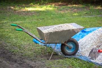 Wheelbarrow in the garden - garden work. Wheelbarrow filled with gravel. Filling a wheelbarrow with...