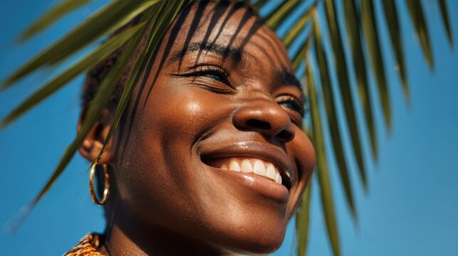 Radiant woman smiling under palm leaves against a clear blue sky