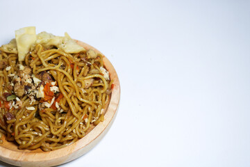 A bowl of spicy fried noodles with wonton crackers in a bowl, isolated on a white background with a wooden plate and traditional chopsticks