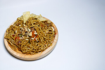 A bowl of spicy fried noodles with wonton crackers in a bowl, isolated on a white background with a wooden plate and traditional chopsticks