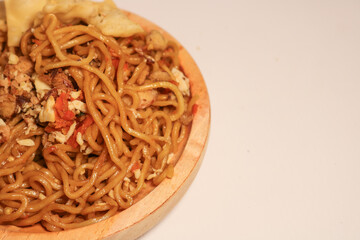 A bowl of spicy fried noodles with wonton crackers in a bowl, isolated on a white background with a wooden plate and traditional chopsticks