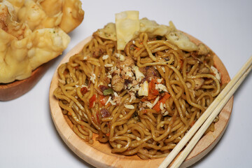 A bowl of spicy fried noodles with wonton crackers in a bowl, isolated on a white background with a wooden plate and traditional chopsticks
