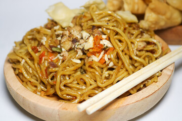 A bowl of spicy fried noodles with wonton crackers in a bowl, isolated on a white background with a wooden plate and traditional chopsticks