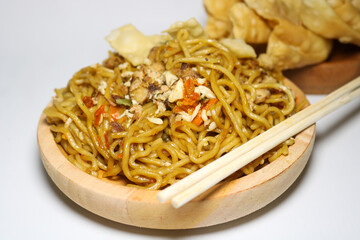A bowl of spicy fried noodles with wonton crackers in a bowl, isolated on a white background with a wooden plate and traditional chopsticks