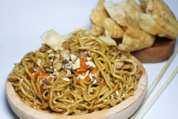 A bowl of spicy fried noodles with wonton crackers in a bowl, isolated on a white background with a wooden plate and traditional chopsticks