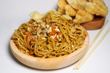 A bowl of spicy fried noodles with wonton crackers in a bowl, isolated on a white background with a wooden plate and traditional chopsticks