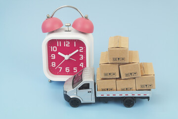 Lorry truck with cardboard boxes and alarm clock on blue background. Shipping and delivery time concept. 
