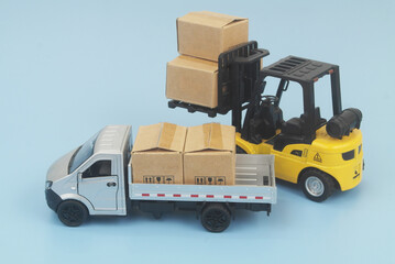Obraz premium Silver lorry truck with cardboard boxes and forklift truck on blue background. Shipping, delivery, cargo, moving and freight transportation concept.