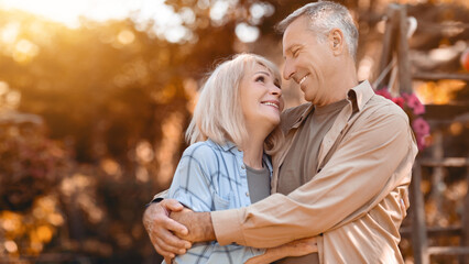 A joyful couple embraces in a beautiful garden filled with autumn colors. They share a loving look while surrounded by nature, capturing the warmth of their connection in a serene setting.