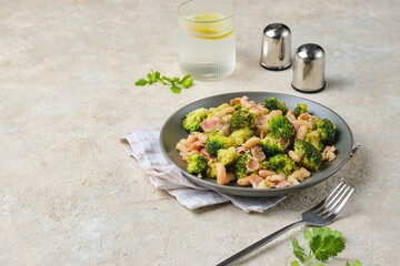 Fried broccoli with bacon and canned white beans on a gray plate against a light concrete background. Broccoli recipes.