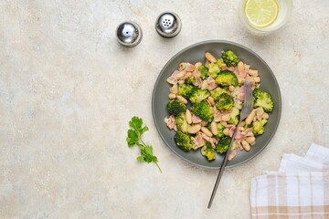 Fried broccoli with bacon and canned white beans on a gray plate against a light concrete background. Broccoli recipes.