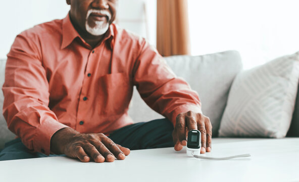 A senior man sits in a cozy living room, holding a pulse oximeter. He appears focused while measuring his heart rate. The relaxed atmosphere enhances his well-being.