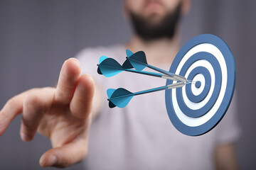 Close-up of a person's hand pointing towards a dartboard with darts successfully hitting the...