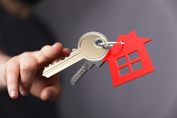 Close-up of a hand holding a key with a red house-shaped keychain. Concept of buying a home, real estate, and property ownership. Perfect for mo