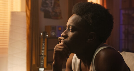 A thoughtful male person sits alone in a cozy living room, facing the window with visible pain and...