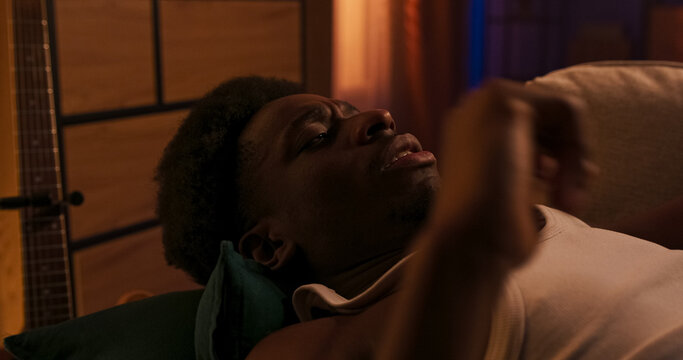 A relaxed male person naps on the couch after a long day, with a blanket covering his body. He is a student, handsome and athletic, preparing to wake gently from sleep.