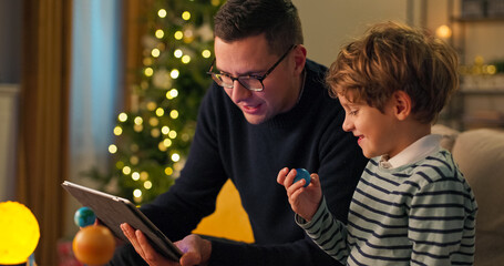 Close-up of seven-year-old boy and dad, who are considering model of the solar system. The boy is holding model of the planet Earth, and father with glasses tells him about it. Boy listens intently.