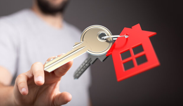 A person's hand holding keys with a house keychain, representing new home ownership and real estate purchase - Powered by Adobe