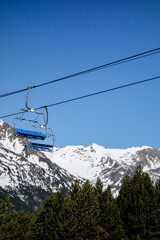 Ski lift high up in the snow capped mountains on a cold bright day with clear blue sky. Chair lifts carry skiers up and down the mountains to where the snow and the skiing is best.