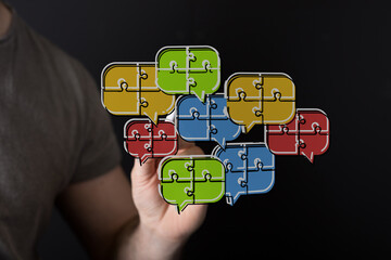 Hand holding speech bubble puzzle pieces connecting to represent collaboration, teamwork, and...