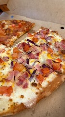 Pizza slices with toppings including cheese, ham, onions, and tomatoes on a cardboard box background