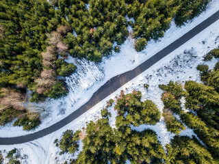 Top-down aerial view of a winding paved road through a snow-covered evergreen forest in winter