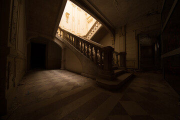 Grand stone staircase in dim neoclassical hall - derelict mansion interior with sunlit stairwell and peeling paint