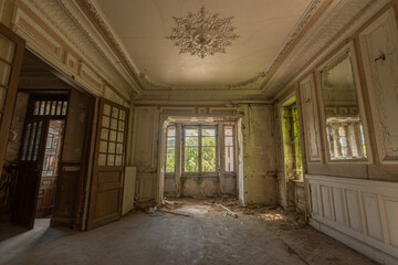 Sunlit abandoned mansion interior with ornate ceiling, peeling paint and elegant decay