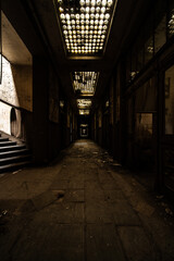 Dimly lit abandoned corridor with patterned skylights, peeling walls and atmospheric vanishing point